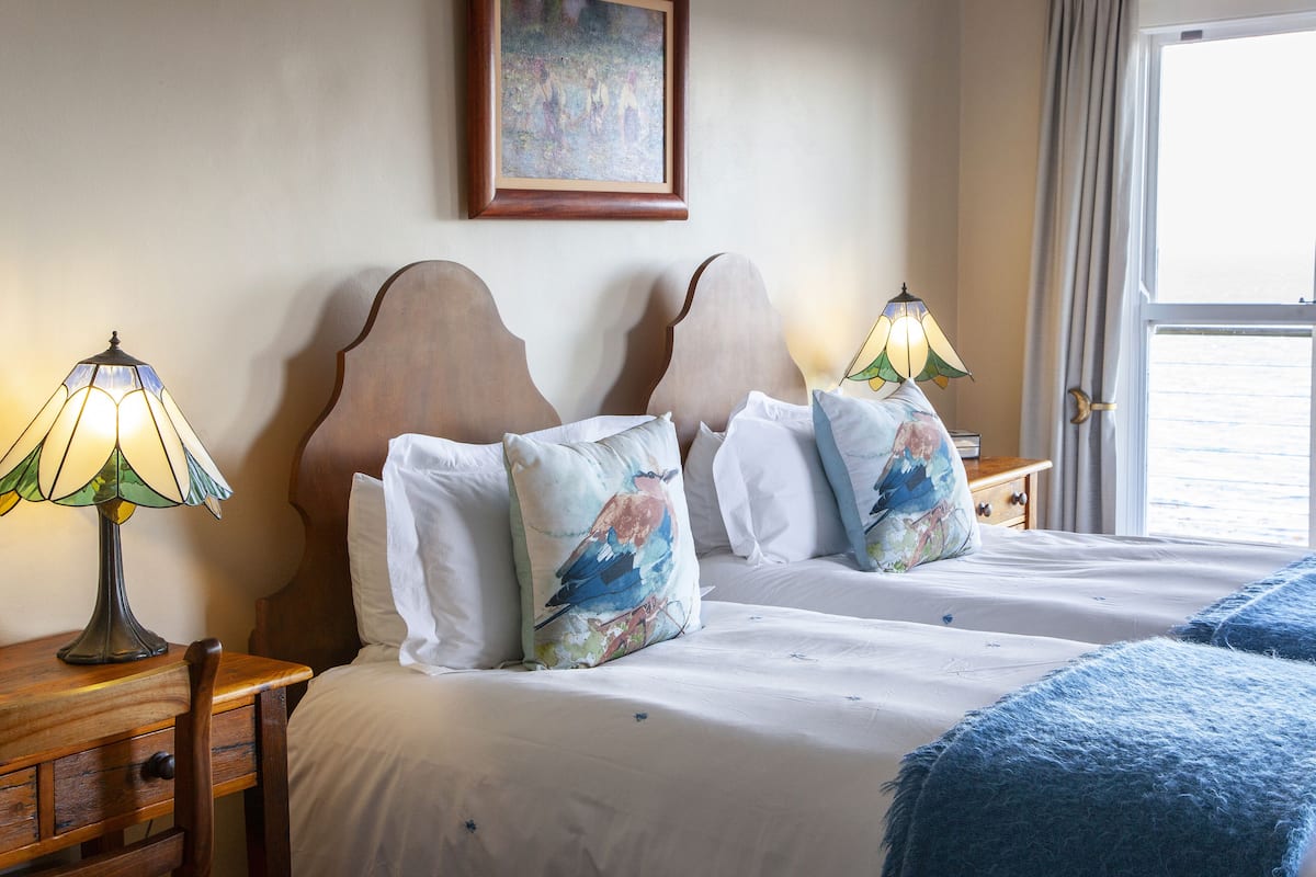 Ein Hotelzimmer mit einem großen Bett, zwei Nachttischen, einem Holzstuhl, einem Bild an der Wand und einem Fenster mit Vorhängen.