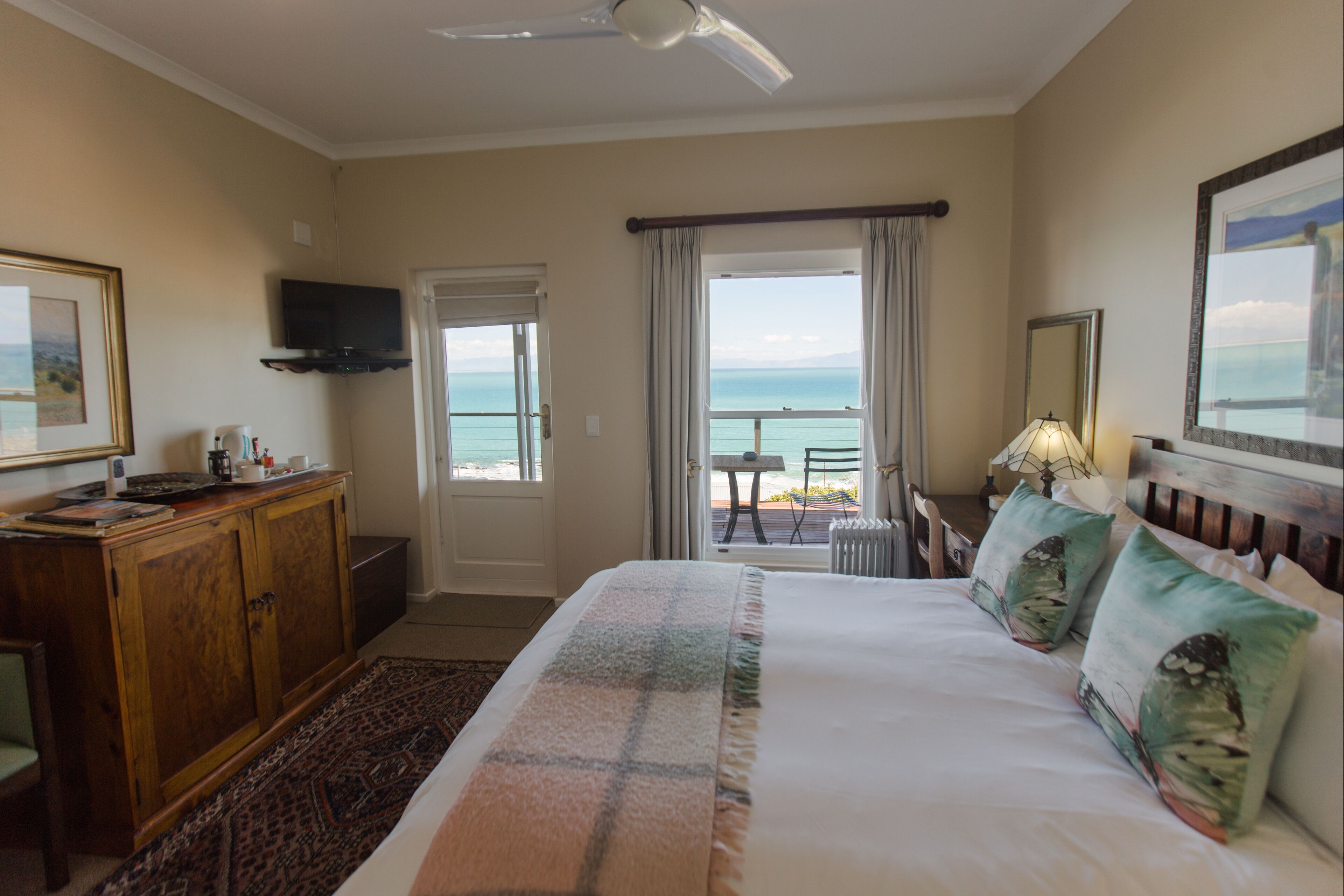 A hotel room with a bed, a desk, a television, a view of the ocean, and a balcony.