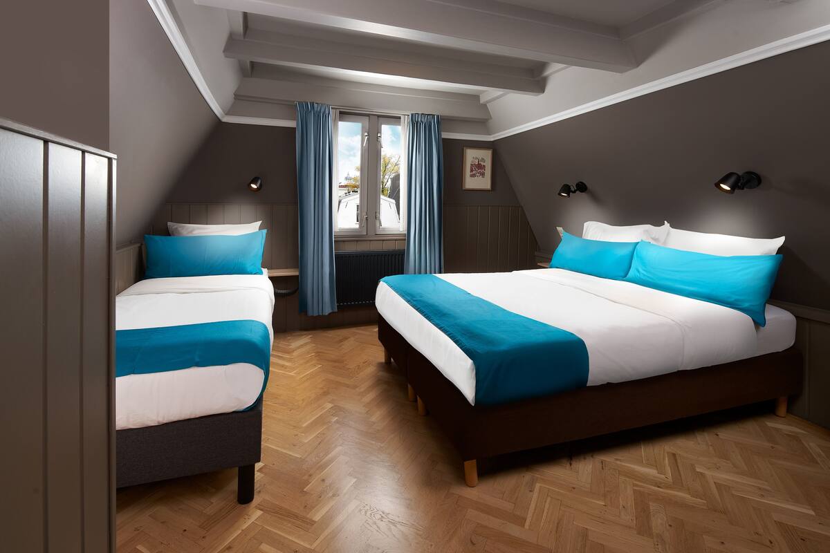 A bedroom with two beds, a window with curtains, and a radiator.