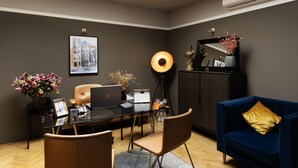 A modern office space with a glass desk, leather chairs, a blue sofa, and a cityscape painting on the wall. - Stanley Collection Hotel Hegra Amsterdam (Amsterdam)