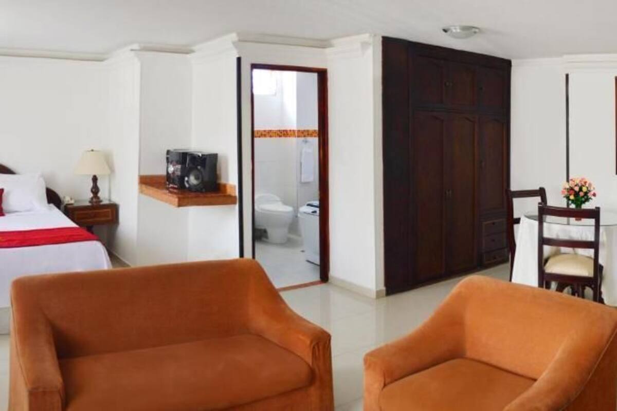 A hotel room with a bed, two chairs, a desk, and a painting on the wall.