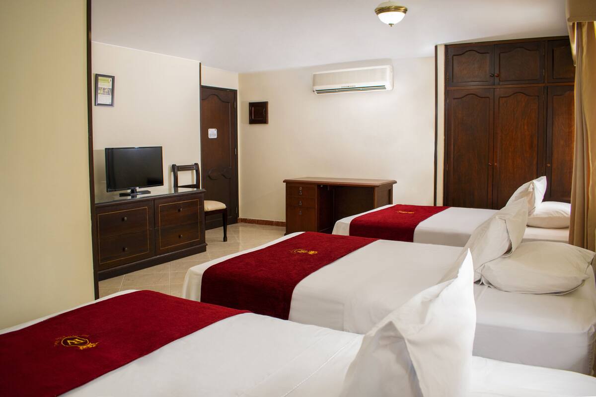 A hotel room with three beds, a TV, a desk, and a wardrobe.
