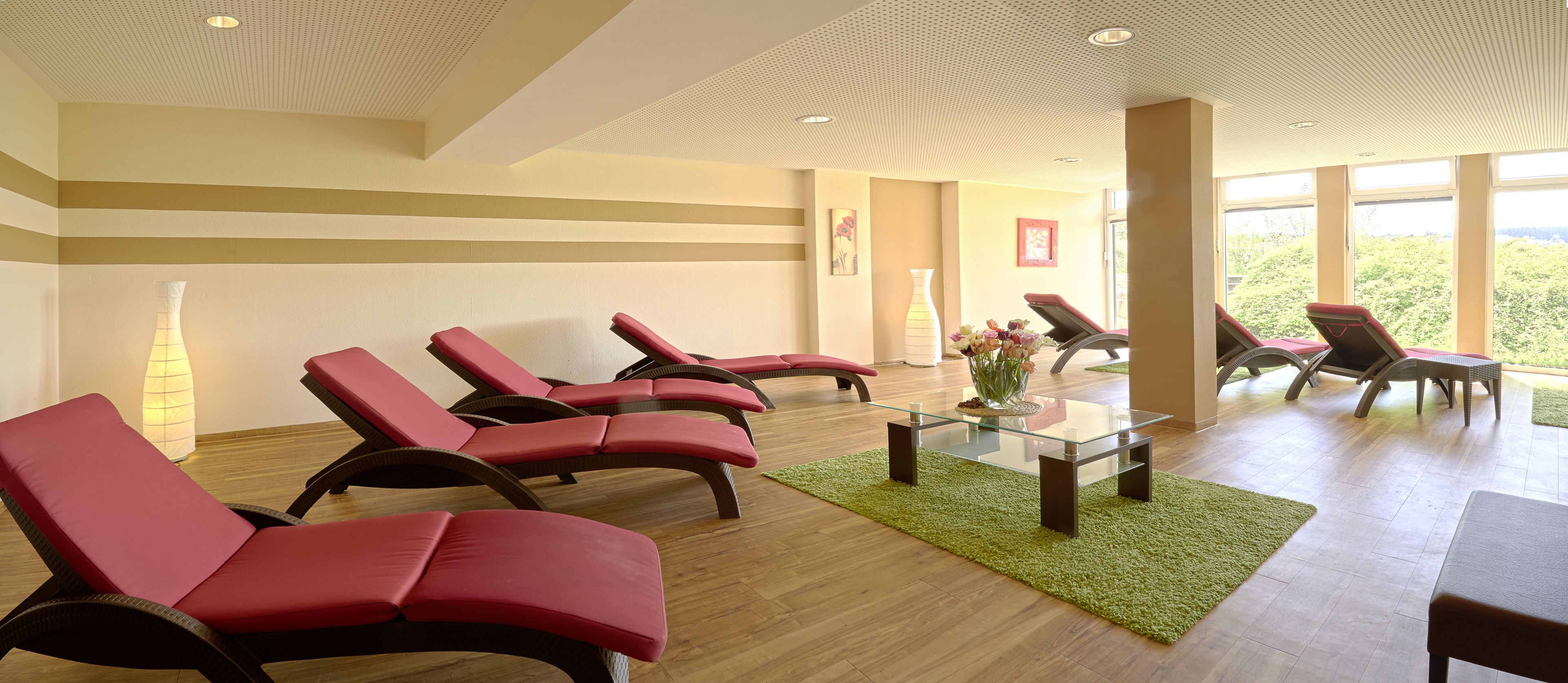 A spa area with red lounge chairs, a glass table, and a green rug.