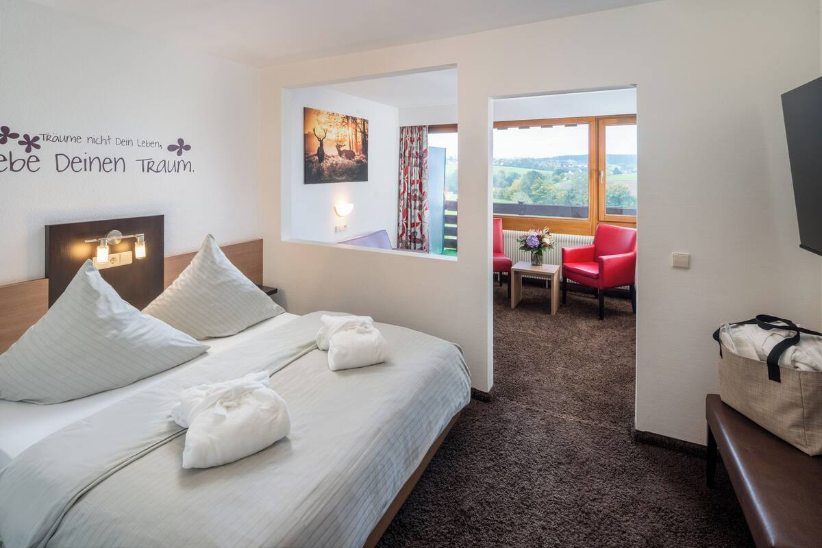 Une chambre d’hôtel équipée d’un lit, d’un bureau, d’une chaise, d’une fenêtre avec vue et d’un mur orné d’une citation inspirante.