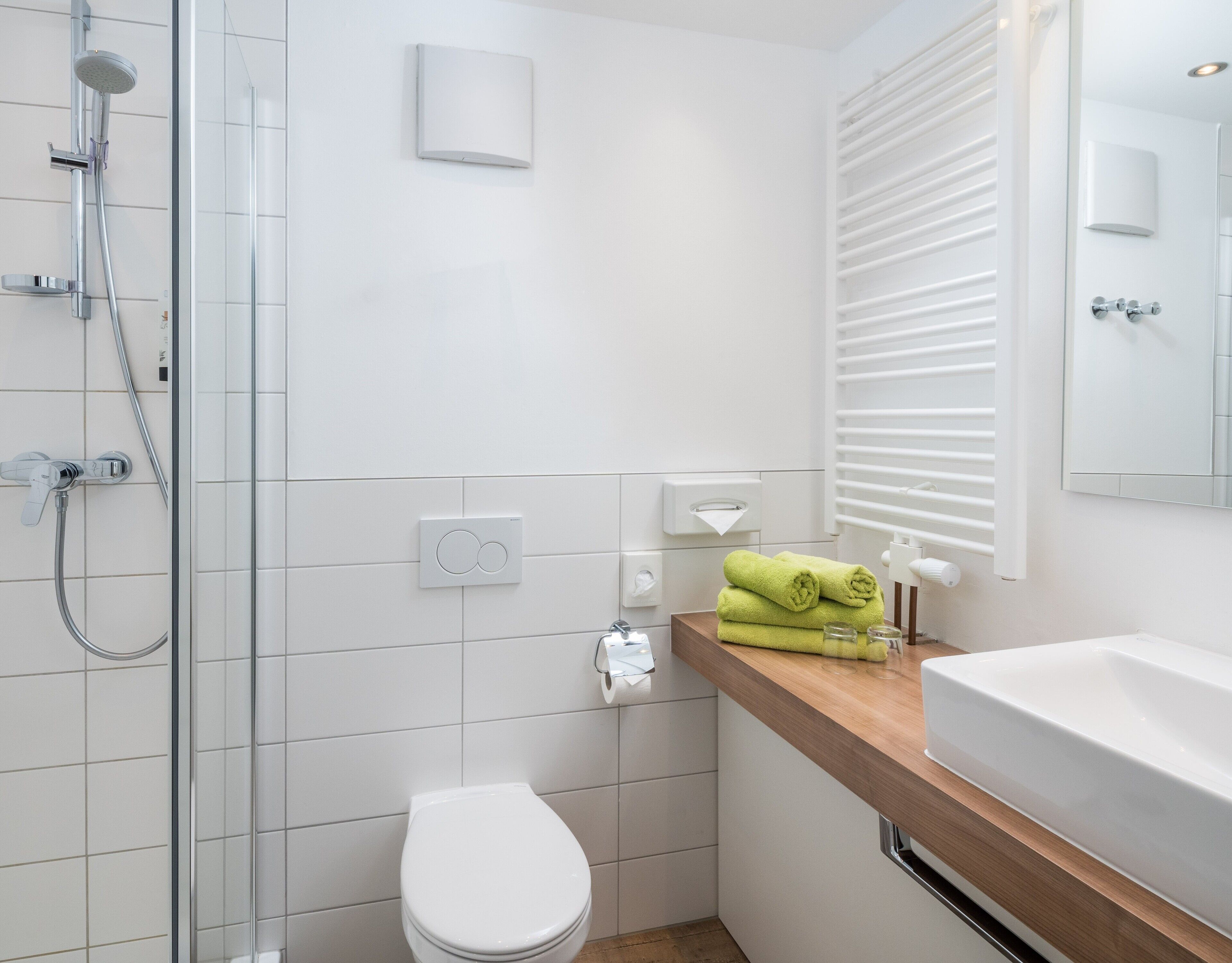 Um banheiro moderno com box de vidro, vaso sanitário branco e toucador de madeira com pia.