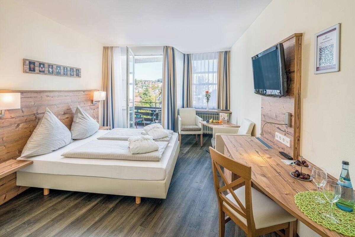 Une chambre d’hôtel avec un lit, un bureau, une chaise, une télévision et une fenêtre avec des rideaux.