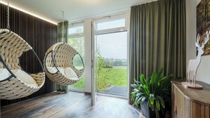Une pièce dotée d’une grande porte-fenêtre coulissante donnant sur un jardin, d’un fauteuil suspendu, d’un meuble en bois et d’une plante en pot.