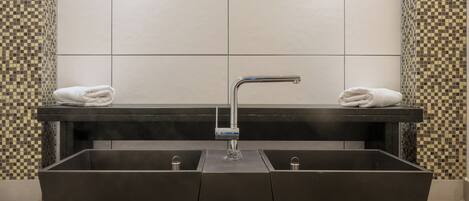 Un baño moderno con un lavabo rectangular grande, dos luces fijadas a la pared y patrones de baldosas de cuadros en las paredes.