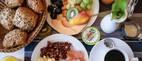 Una mesa de desayuno con pan, frutas, huevos, tocino, salmón y café.