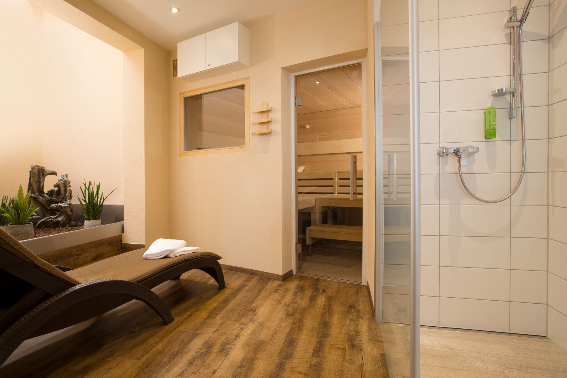 A modern bathroom with a wooden floor, a glass shower enclosure, and a bench with towels.
