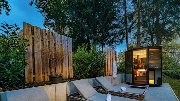Un espace de détente extérieur moderne, comprenant deux chaises longues, une petite structure en verre et une clôture en bois.