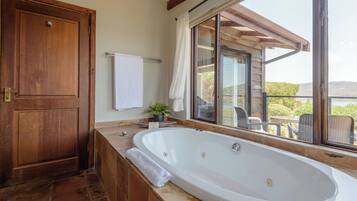 A bathroom with a large bathtub, a wooden door, a towel rack, and a window with a view of the outdoors.
