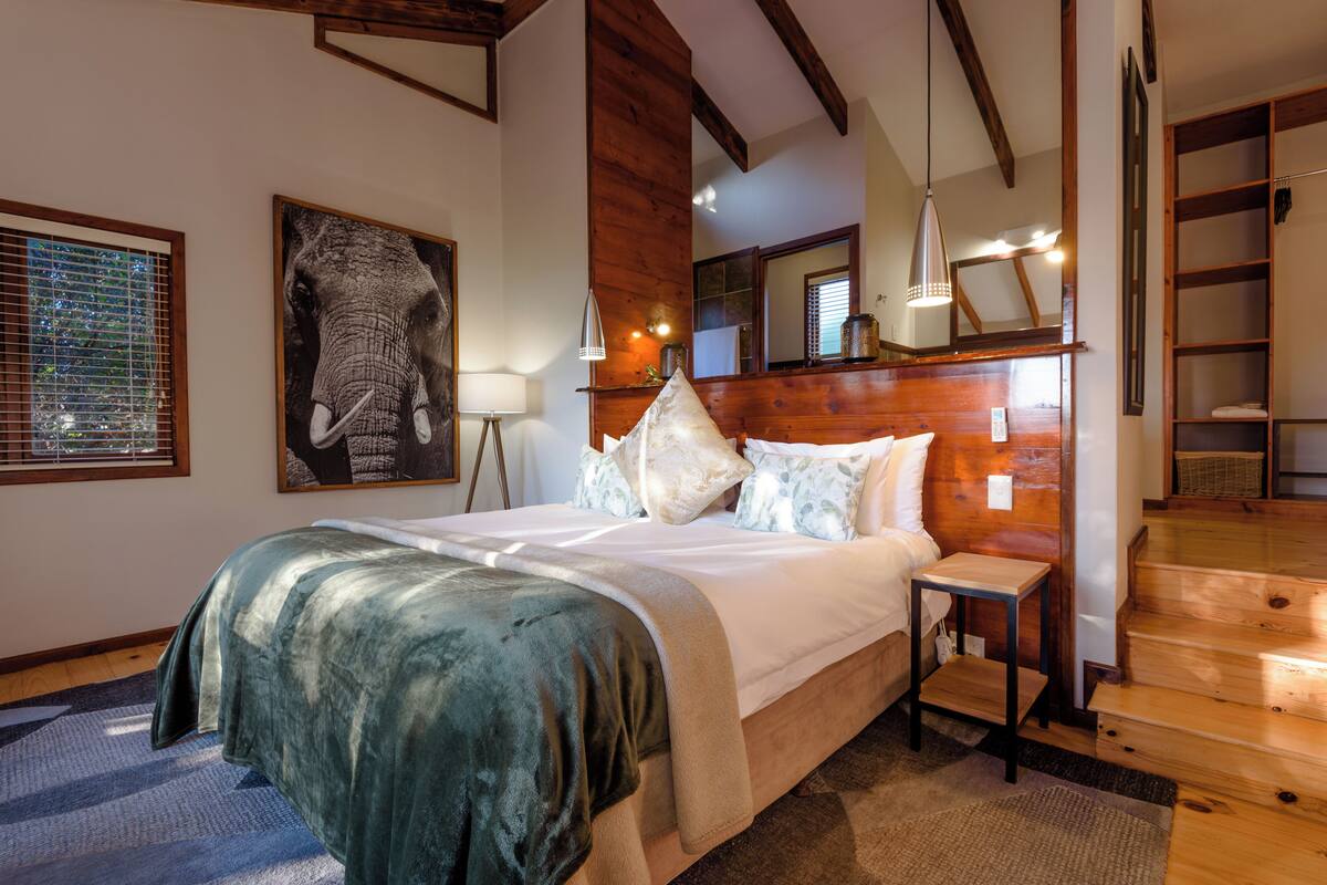 A bedroom with a large bed, a nightstand, a wooden headboard, a mirror, and a staircase.