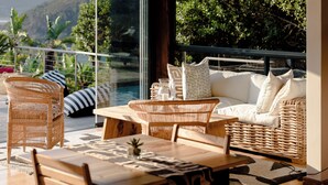 A balcony with wicker furniture, a table, and a view of a mountain and greenery. - Elephant Hide of Knysna Guest Lodge (Knysna)