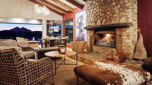 A cozy living area with a stone fireplace, wicker furniture, and a view of the mountains. - Elephant Hide of Knysna Guest Lodge (Knysna)