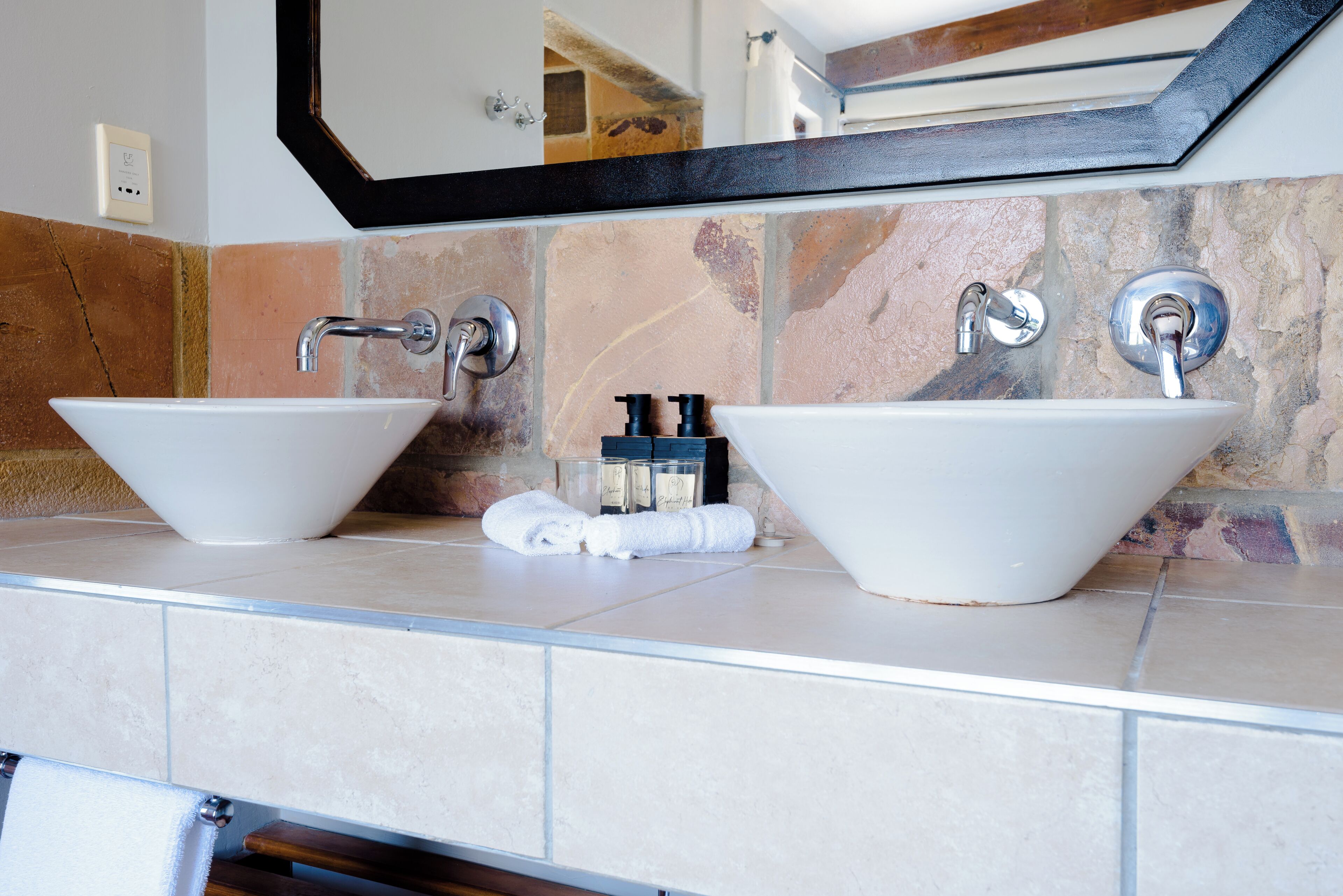 A bathroom with two white vessel sinks, a mirror above, and a towel rack with towels.