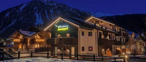A hotel with a sign reading "Residence Neugästei" in a mountainous area at night.