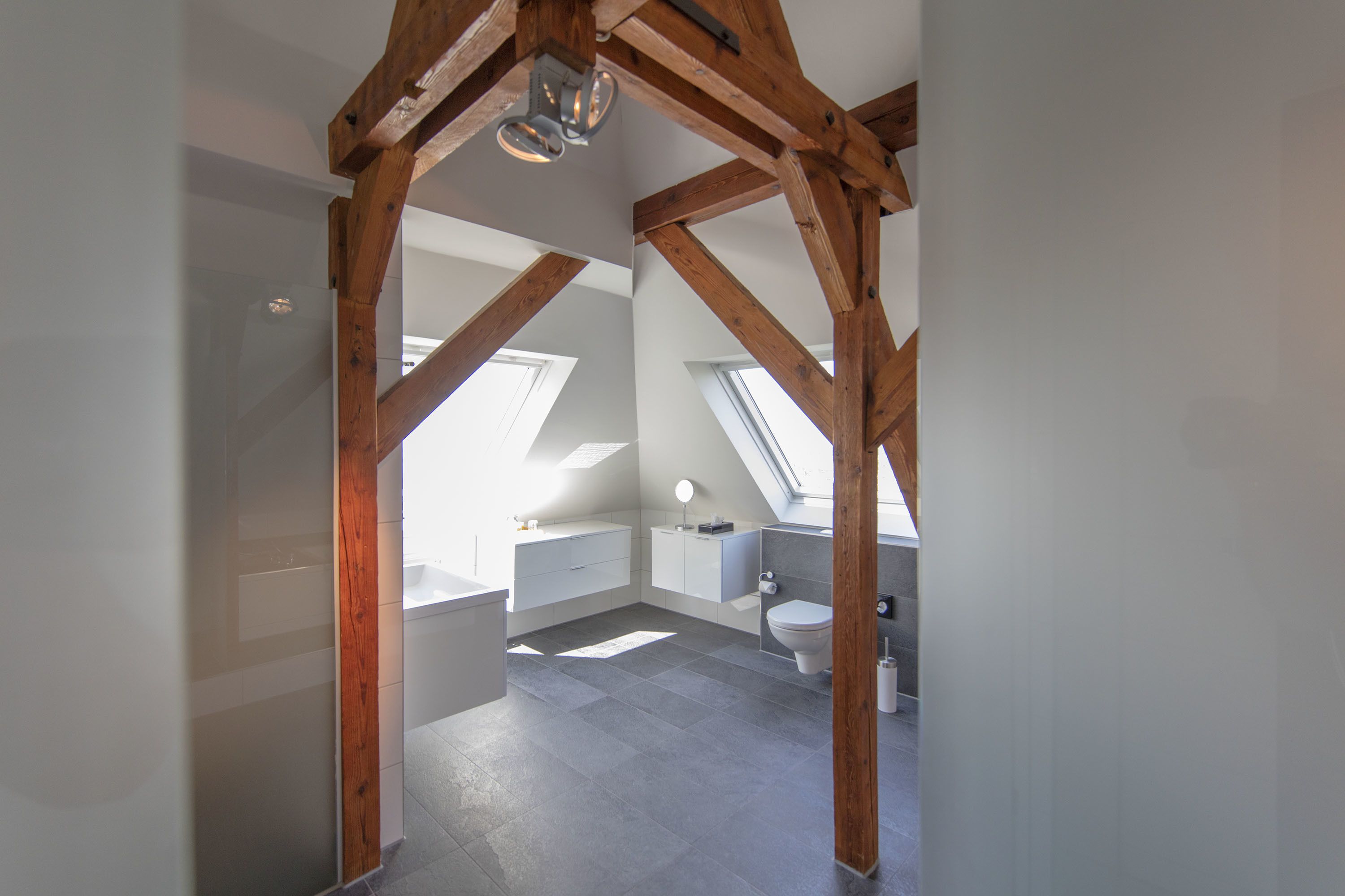 Une salle de bain moderne avec des fenêtres de toit, un plafond en bois et un lavabo blanc.