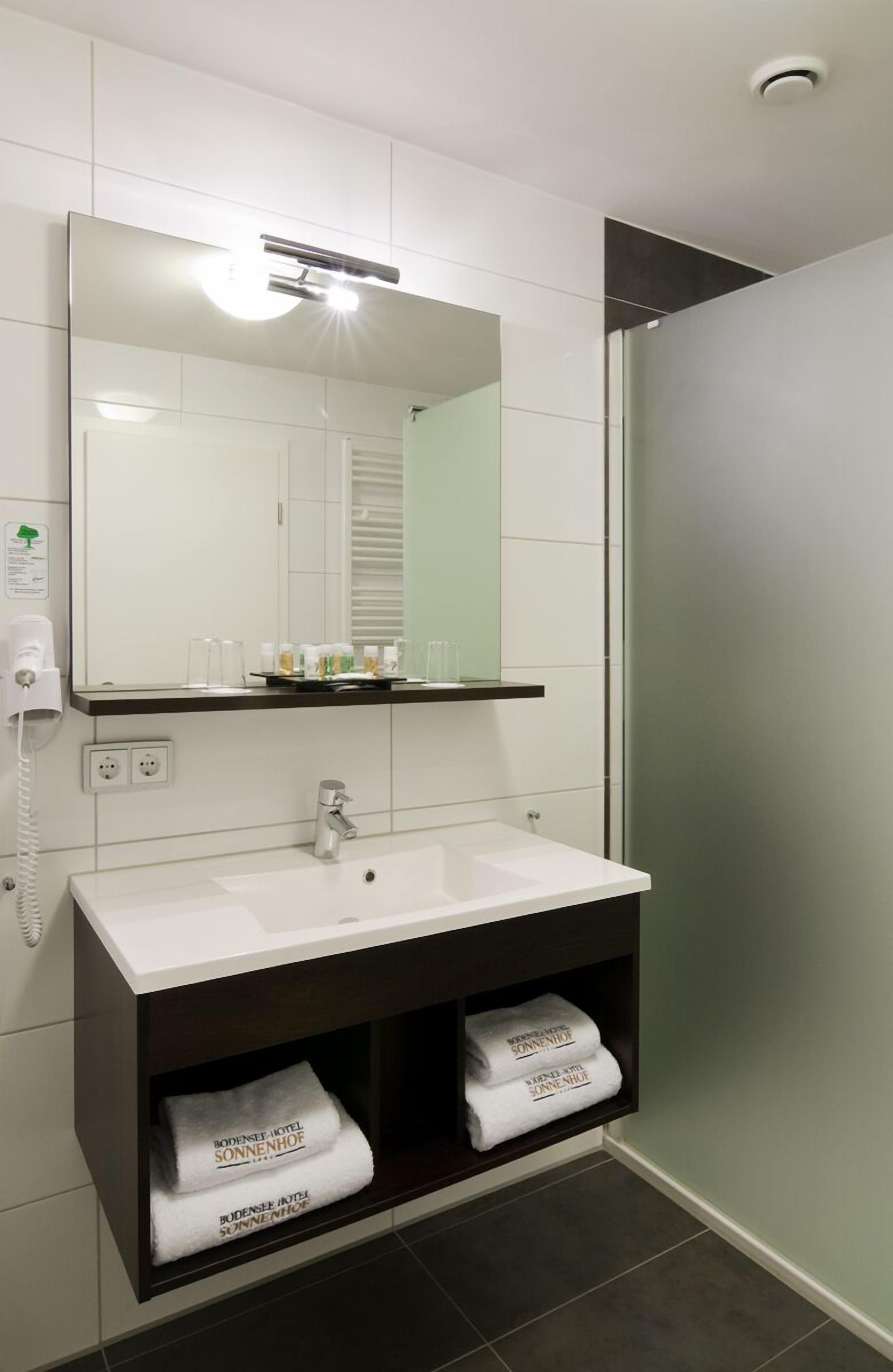 A modern bathroom with a large mirror, white sink, and a towel rack with towels.