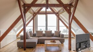 A loft-style room with a wooden beam ceiling, a sectional sofa, a coffee table, and a flat-screen TV. - Bodensee Hotel Sonnenhof (Kressbronn)