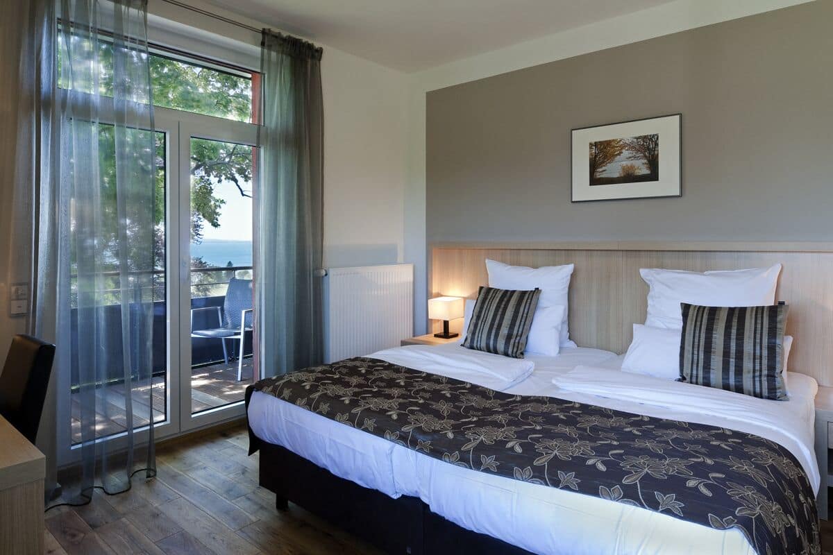 Een slaapkamer met een groot bed, een nachtkastje, een stoel en uitzicht op de natuur door een glazen deur.