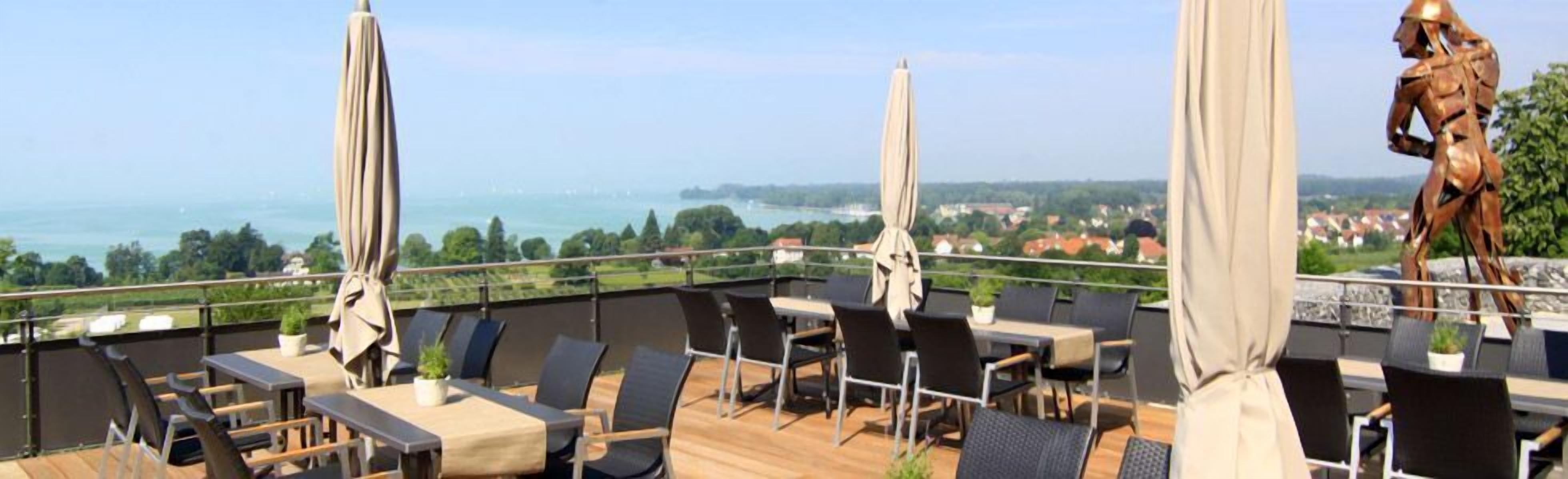 A rooftop terrace with outdoor seating, a statue, and a scenic view of the sea and landscape.
