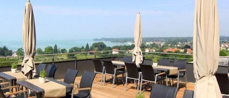 A rooftop terrace with outdoor seating, a statue, and a scenic view of the sea and landscape.