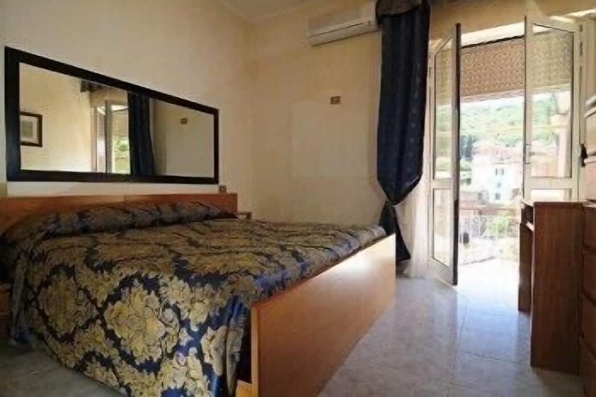 A bedroom with a bed, a large mirror, and a view of the outside.