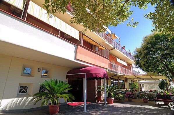 A hotel with a red awning, outdoor seating, and potted plants.
