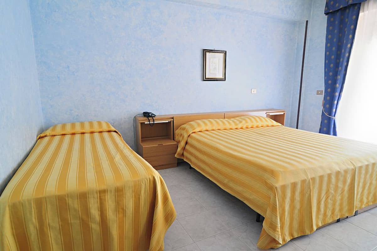 A room with two beds, a nightstand, a framed picture on the wall, and a window with curtains.