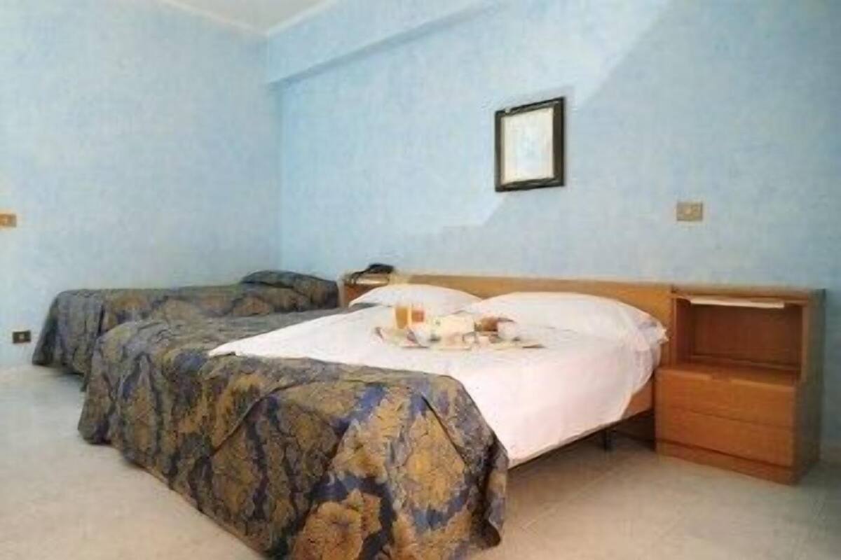 A room with two beds, a wooden nightstand, and a framed picture on the wall.