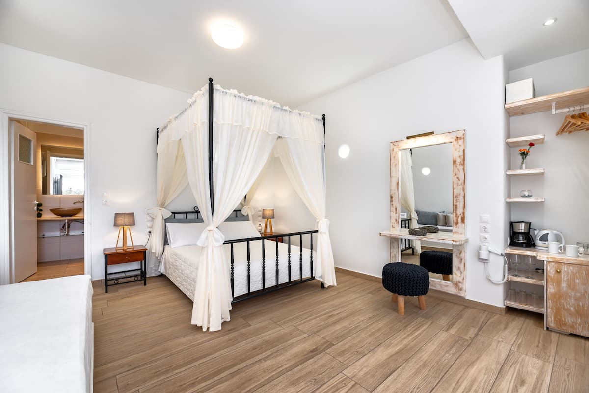 A bedroom with a four-poster bed, bedside tables, a vanity with a mirror, and a wooden floor.