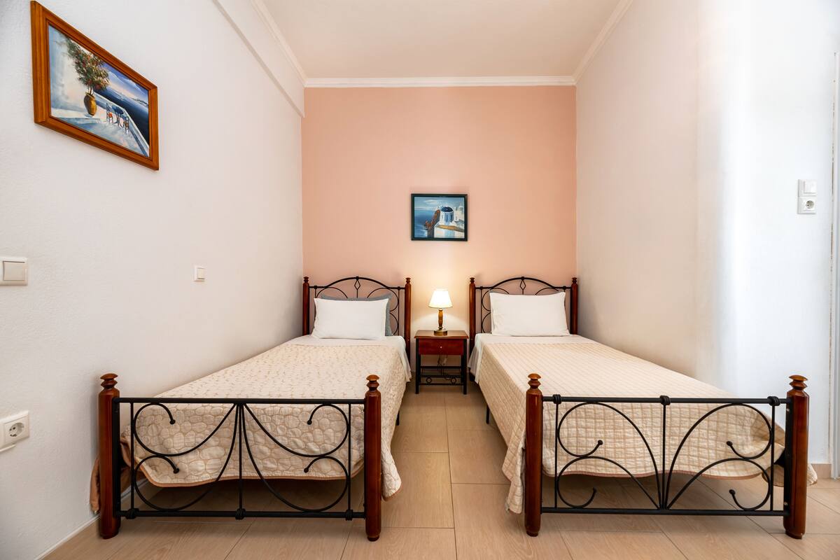 A bedroom with two single beds, a nightstand with a lamp, and a framed picture on the wall.