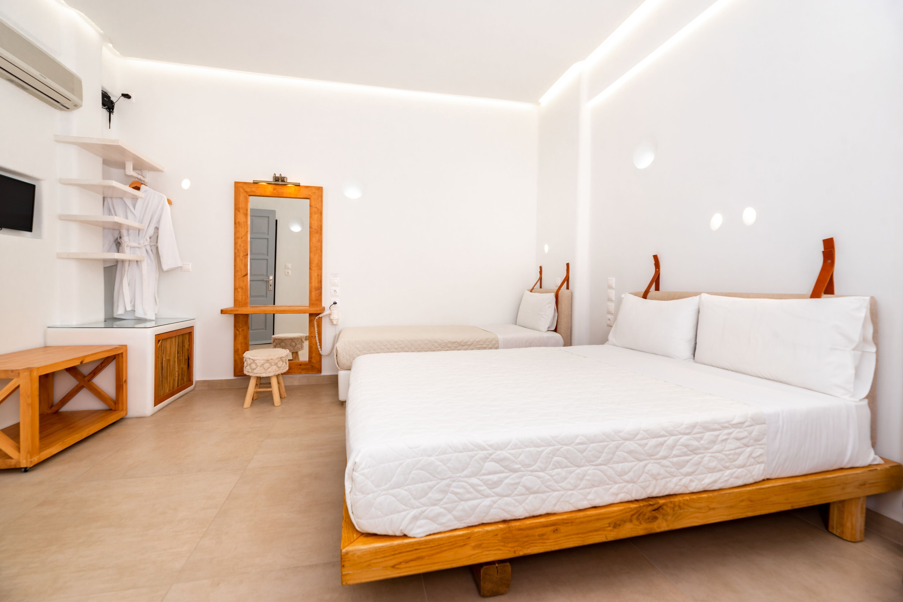 A bedroom with a wooden bed, a small stool, a chair, a mirror, and a TV on a shelf.
