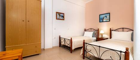 A bedroom with two single beds, a wooden wardrobe, a small table, and two wall-mounted pictures.