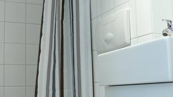 A bathroom with a toilet, a shower curtain, and a wall-mounted faucet.