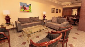 A hotel room with two sofas, a glass coffee table, and wicker chairs. There are two lamps on side tables, a painting on the wall, and a kitchen area in the background. - Rede Andrade Hotel Canadá (Rio de Janeiro)