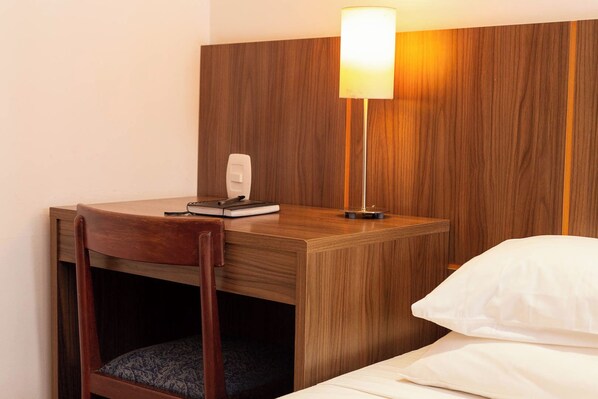 A hotel room with a wooden desk, a chair, a bedside table, a lamp, a notepad, and a pillow. - Rede Andrade Hotel Canadá (Rio de Janeiro)