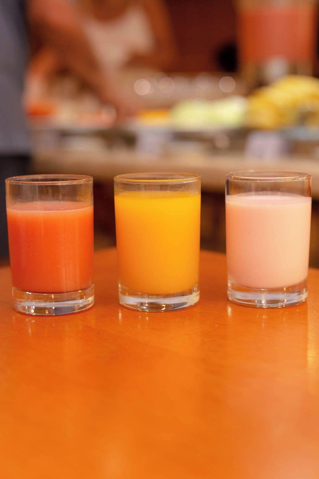 Trois verres de jus sur une table en bois.