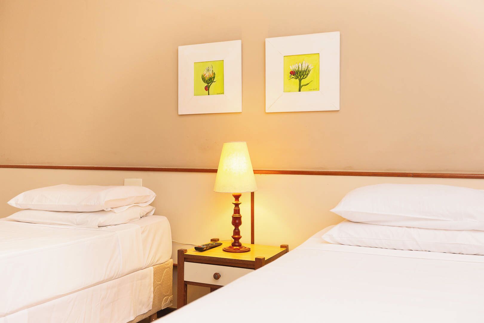 Ein Hotelzimmer mit zwei Einzelbetten, einem Nachttisch mit Lampe und zwei gerahmten Bildern an der Wand.