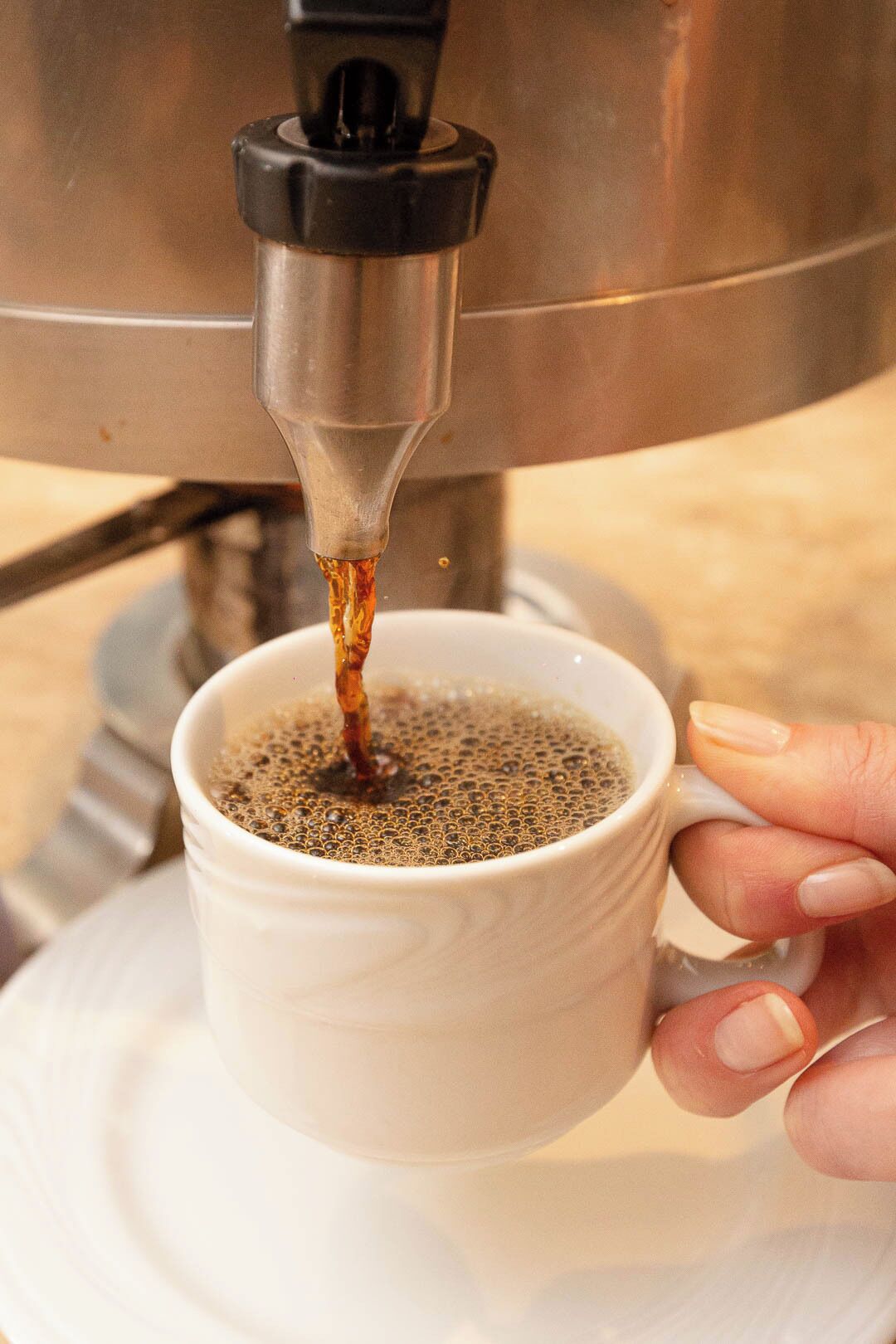 Une main tenant une tasse blanche sous une machine à café, tandis que du café est versé dans la tasse.