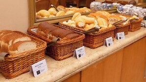 A bakery display with various types of bread in wicker baskets, labeled with names and prices. - Rede Andrade Hotel Canadá (Rio de Janeiro)