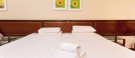 Habitación de hotel con una cama grande, dos almohadas, una toalla enrollada y dos girasoles enmarcados en la pared.