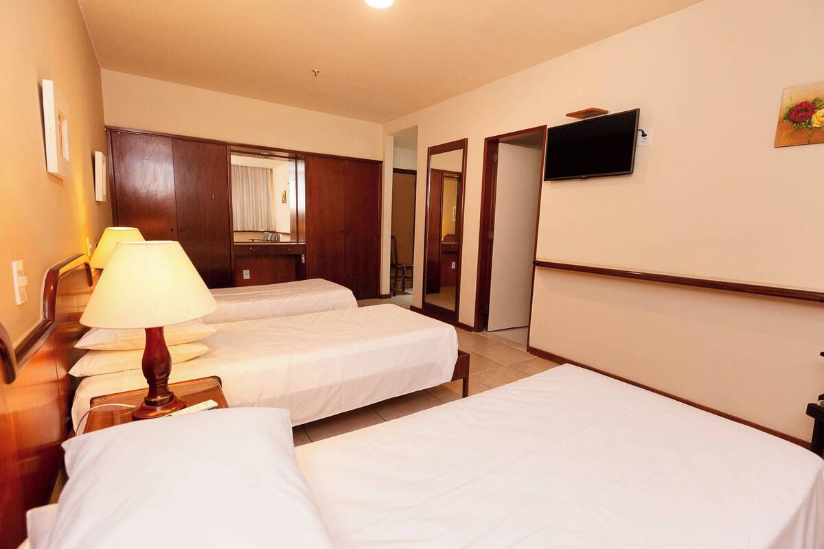 Una habitación de hotel con dos camas individuales, un escritorio con lámpara, un televisor montado en la pared y un espejo.