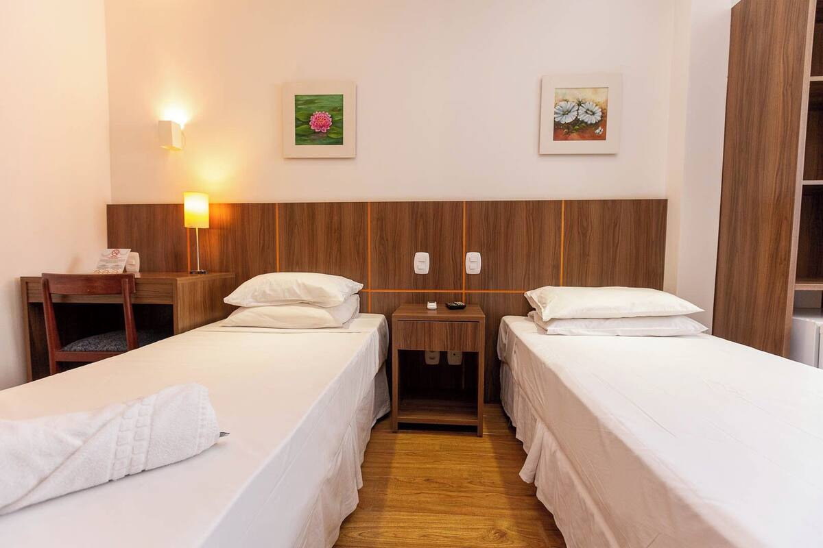 Una habitación de hotel con dos camas individuales, cabeceros de madera, un escritorio con silla y dos lámparas de pared.