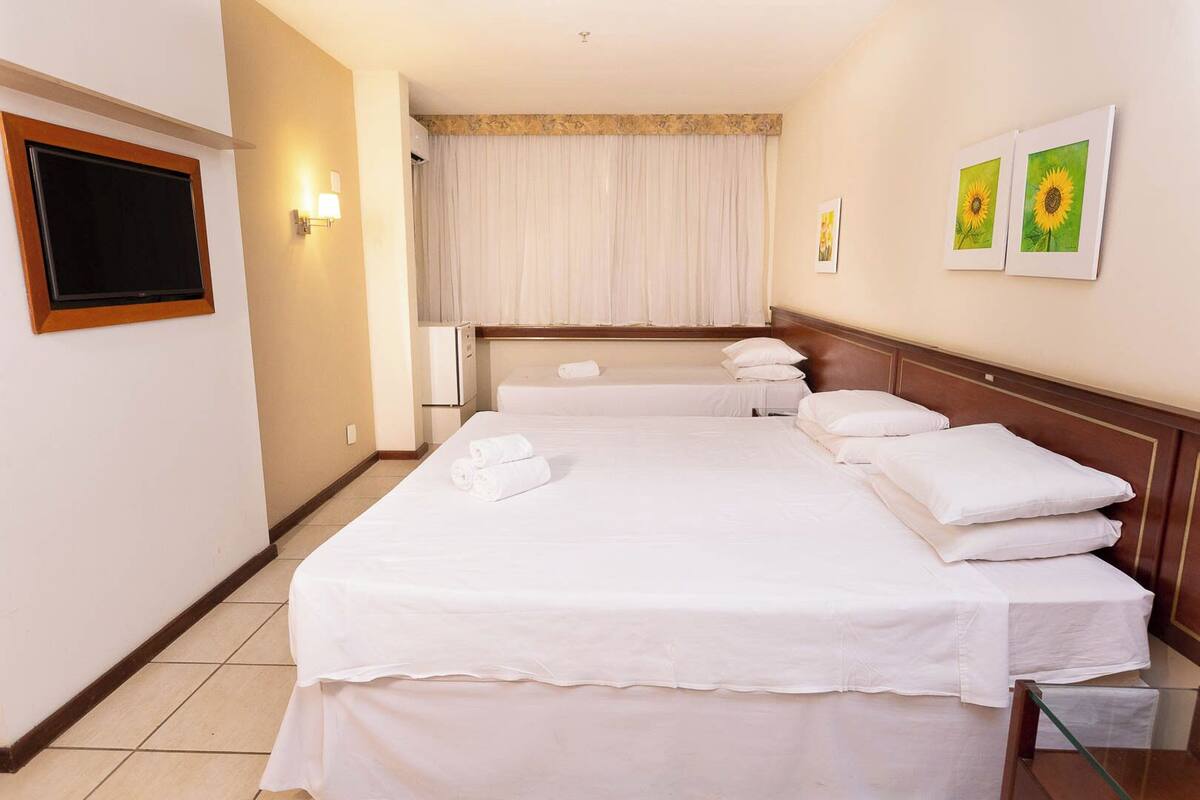 Una habitación de hotel con una cama grande, un televisor de pantalla plana, un minibar y dos cuadros en la pared.