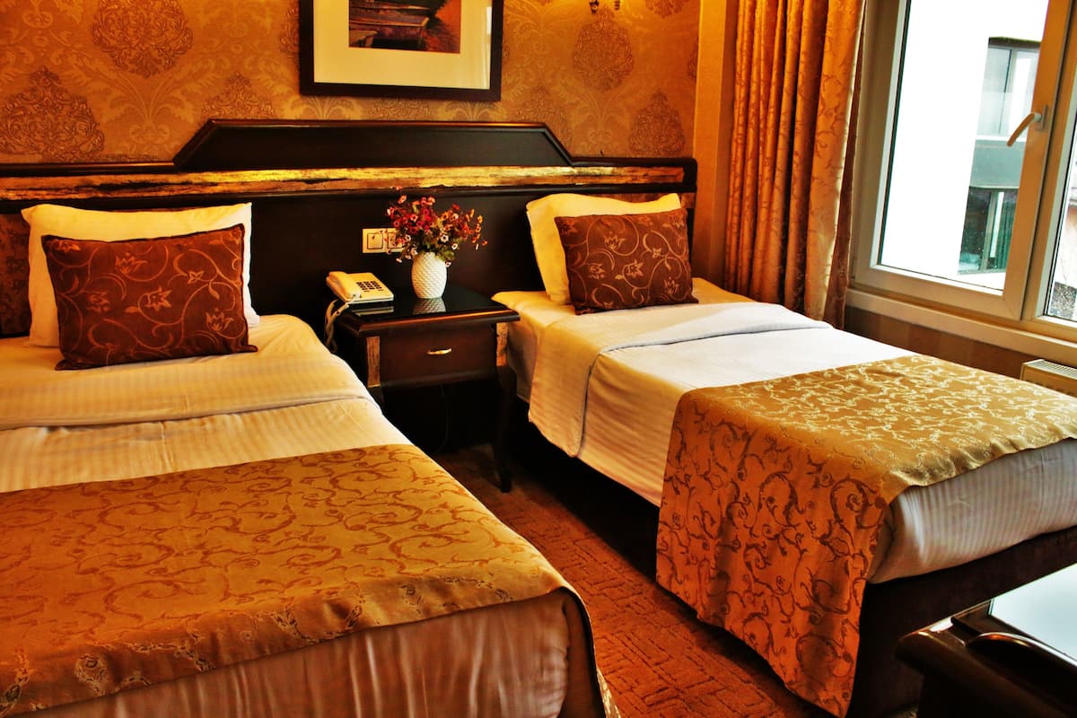 A hotel room with two beds, a nightstand with a vase of flowers, a framed picture on the wall, and a window with curtains.