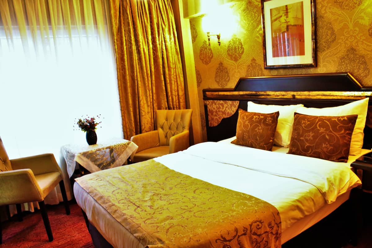 A hotel room with a large bed, a chair, a small table, and a nightstand.