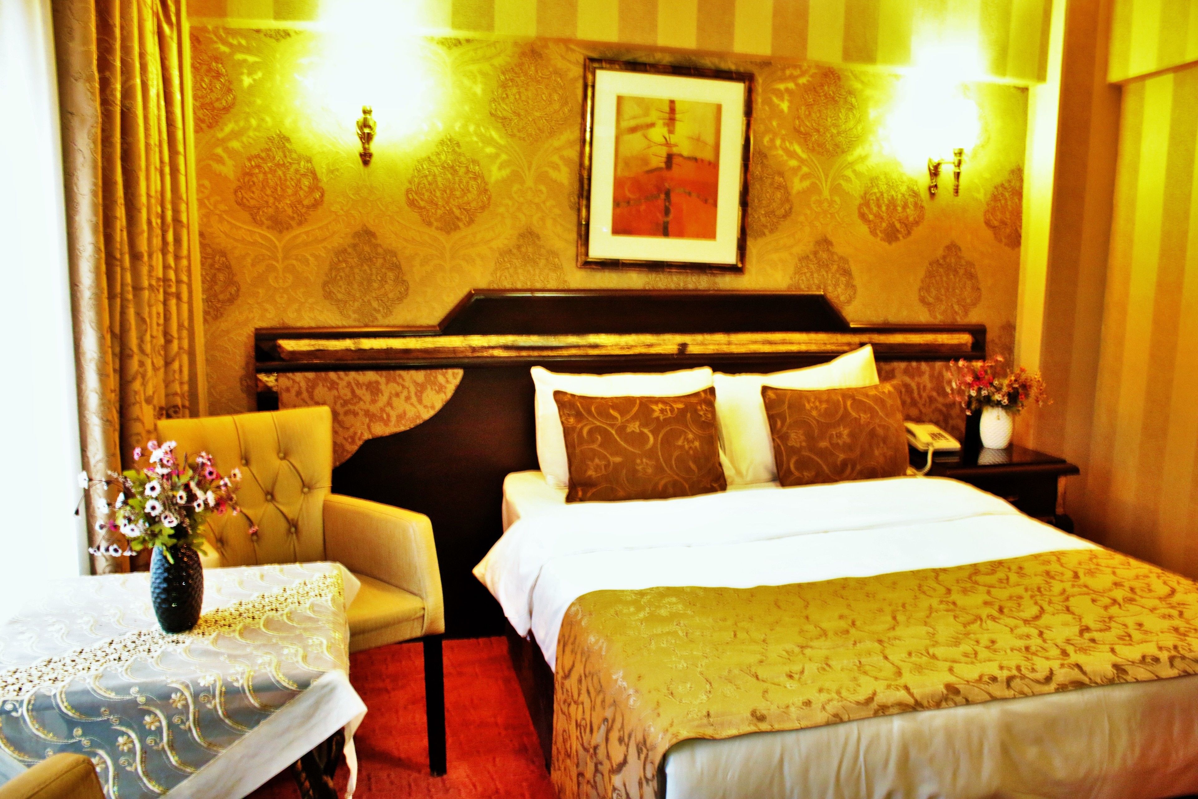 A hotel room with a bed, a chair, a table with a vase of flowers, and a framed picture on the wall.