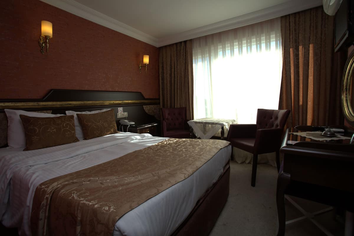 A hotel room with a large bed, a desk, a chair, and a small table.